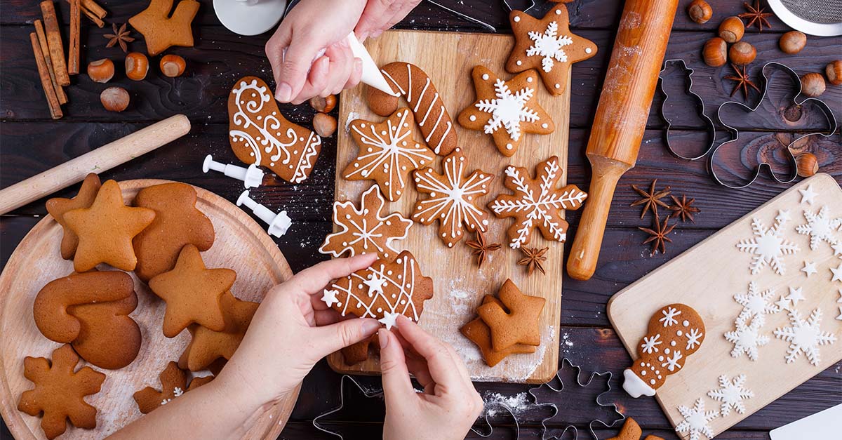 A couple of people decorating gingerbread cookies with icing (close up on the cookies).